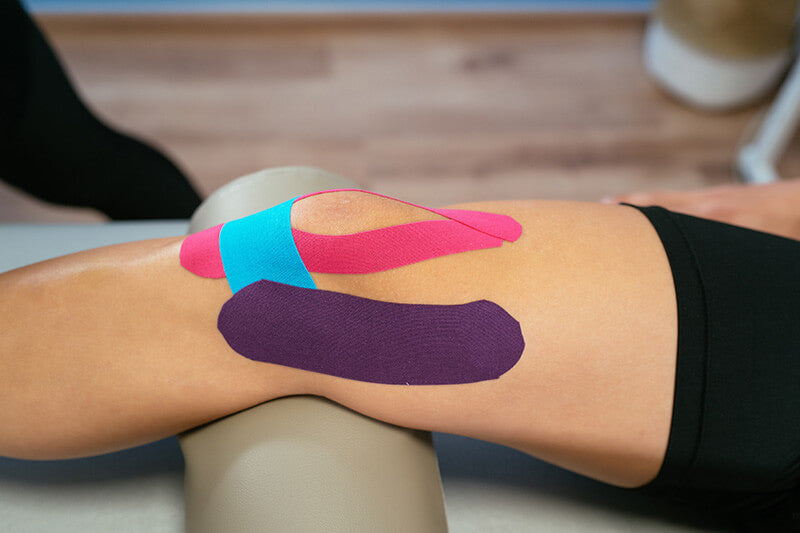 Sporttape wordt door een therapeut op het been van een persoon aangebracht